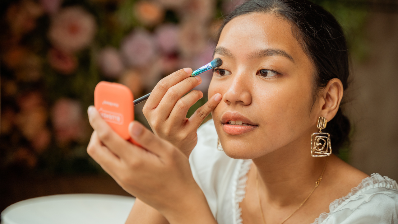 Image of a woman using a small mirror to apply eyeshadow
