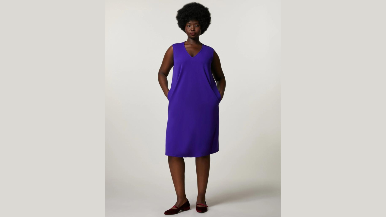 A photo of a black woman in a blue sundress and sandals, posing for the camera. The theme is about how to beat the heat and dress with ease in the office

