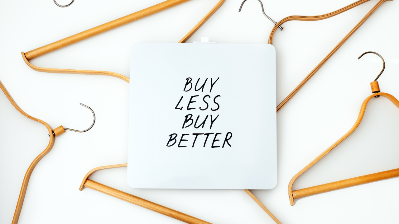 A picture of hangers arranged in a random pattern, with a sign in the middle saying "Buy Less, Buy Better."