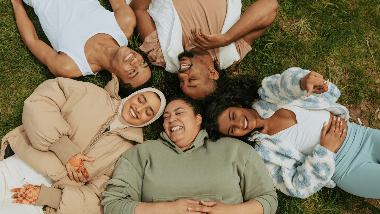 Image of a diverse group of people lying on the ground in a circle and smiling.